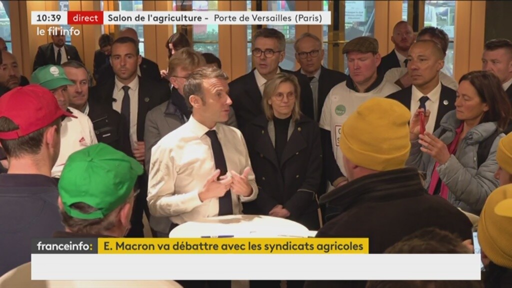 Macron en chemise et cravate devant un mange-debout, avec des ministres derrière et des gen autour.